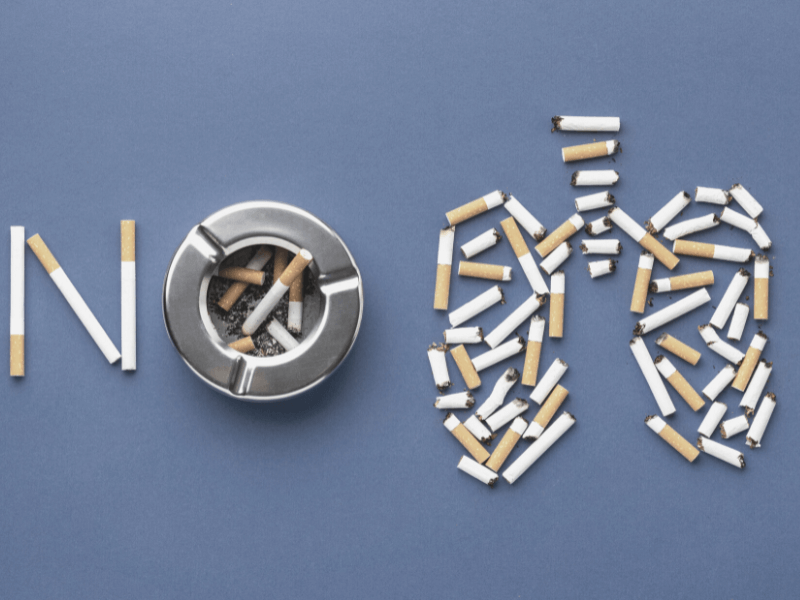 The word NO and a pair of human lungs laid out in cigarettes. The O from NO is formed by a grey circular ashtray. The words are on a blue-grey background